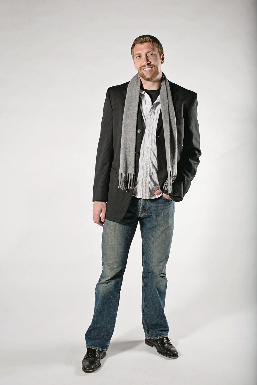 Muž v saku a košeli sa usmieva, oblečený v džínsoch a šále.