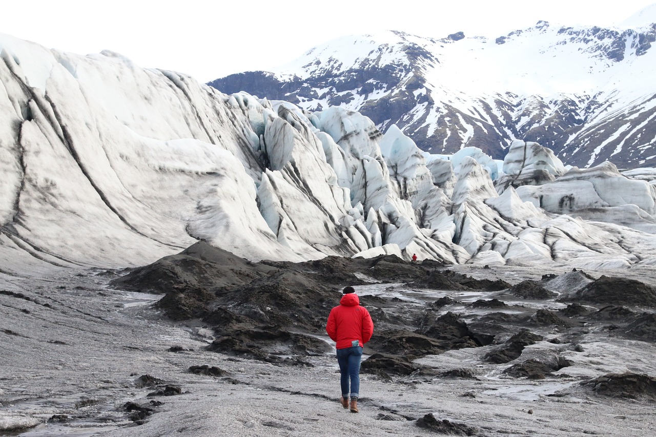Muž v červenej vetrovke kráča po ľadovci, turistika.