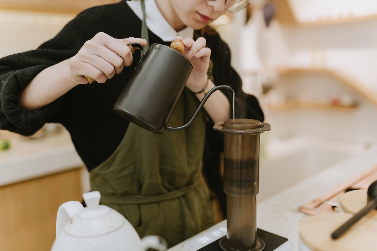 Osoba v zelenej zástere pripravuje kávu pomocou aeropressu.