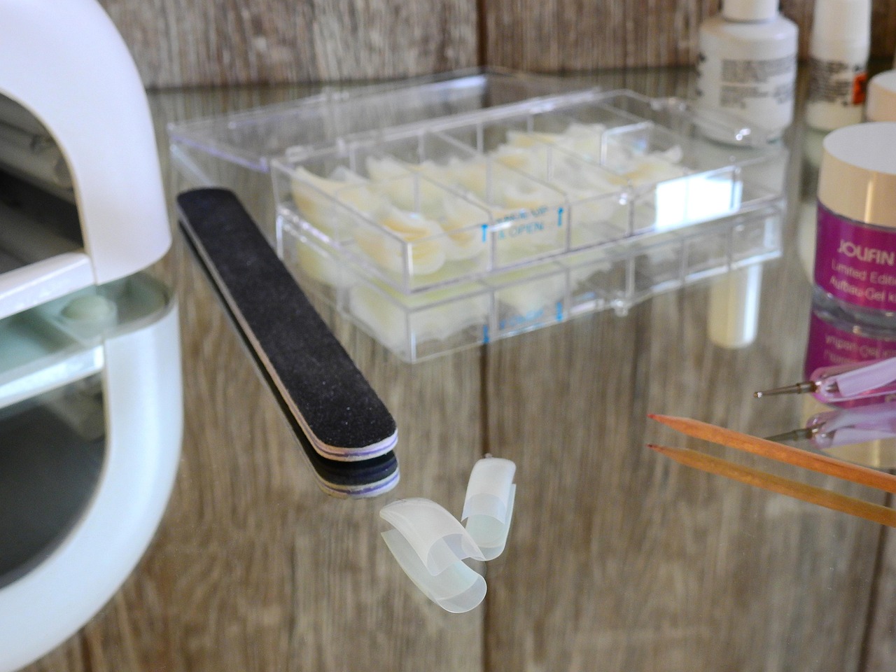 Fotografia zobrazuje pomôcky na aplikáciu gélových nechtov, vrátane UV lampy, pilníka a tipov.