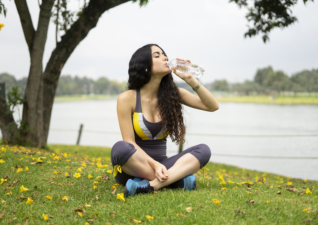 Žena sedí na tráve a pije vodu z fľaše.