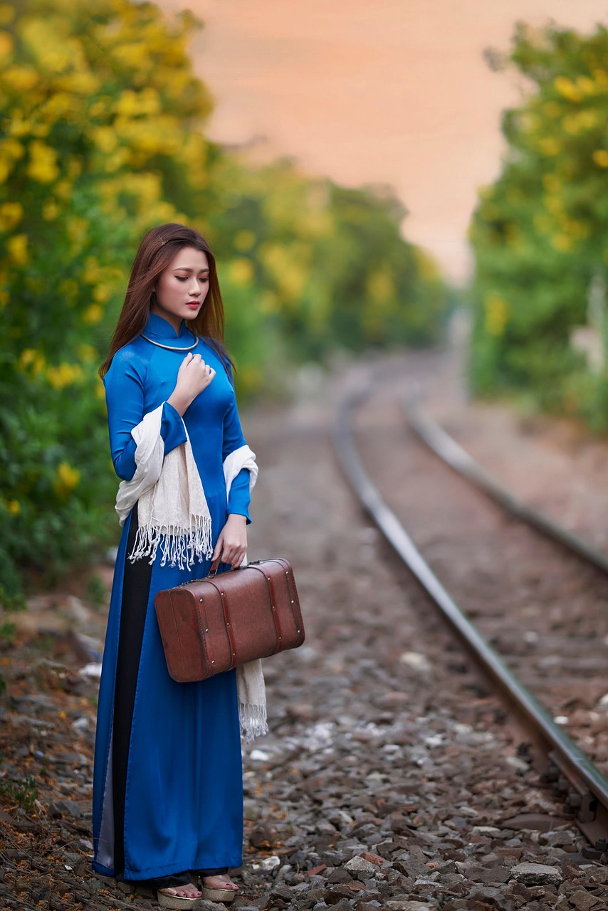 Žena v modrých šatách s elegantnou kabelkou a šatkou na železničnej trati.