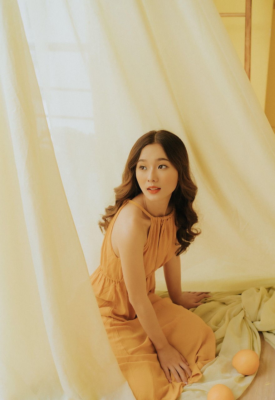 Žena s hnedými vlasmi sedí v žltých šatách.