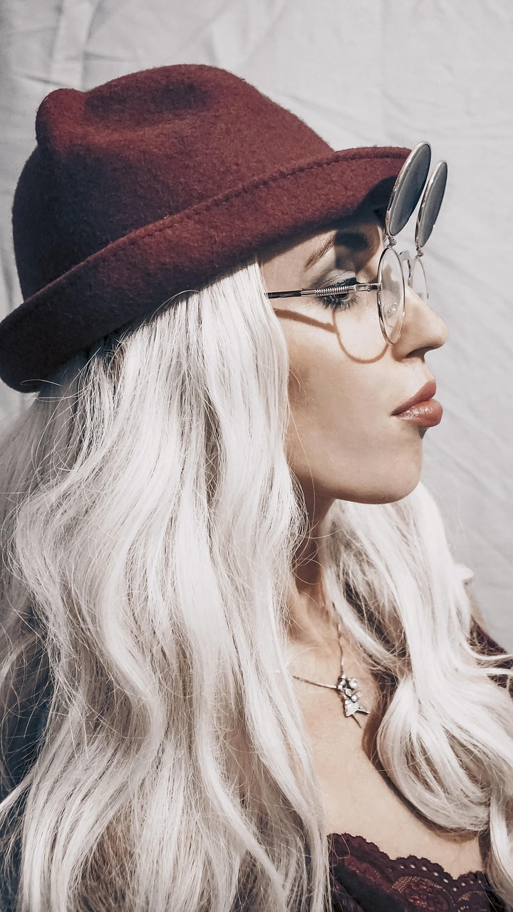 Žena s blond vlasmi, klobúkom a okuliarmi.