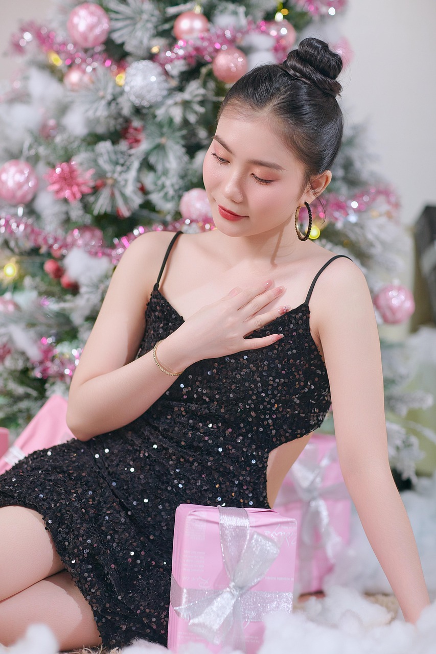 Žena v čiernych šatách sedí pri vianočnom stromčeku.